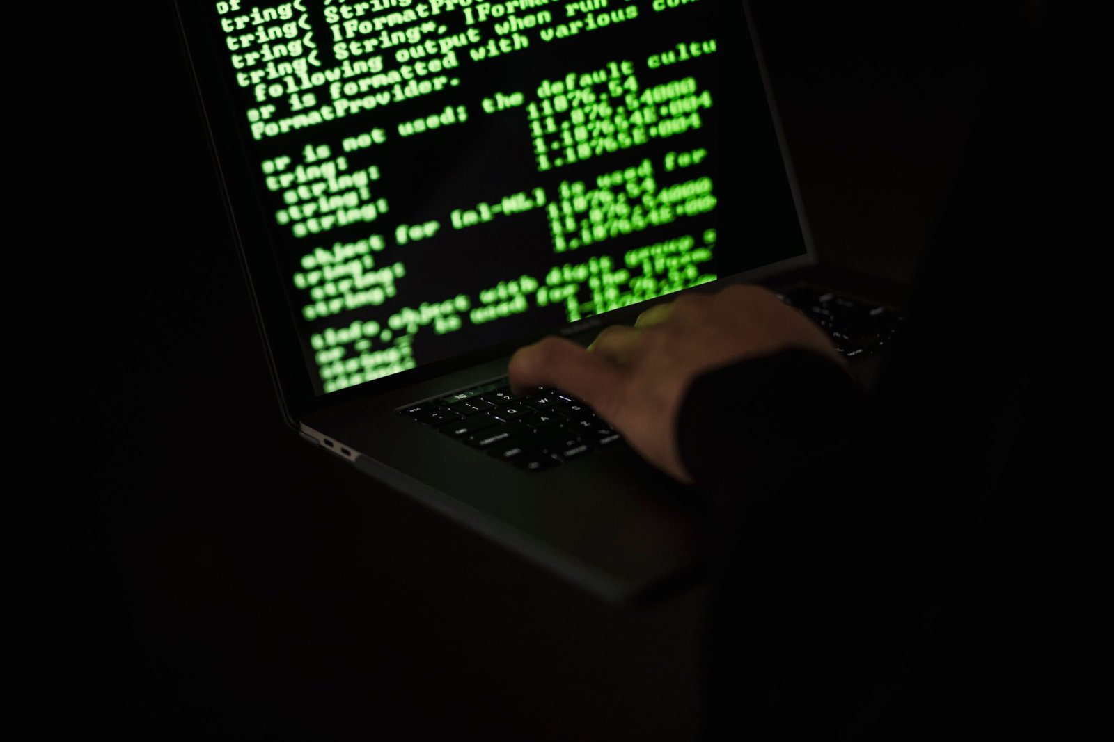 Silhouette of hands typing on a laptop with code on screen, representing Cyber Essentials certification for a small business