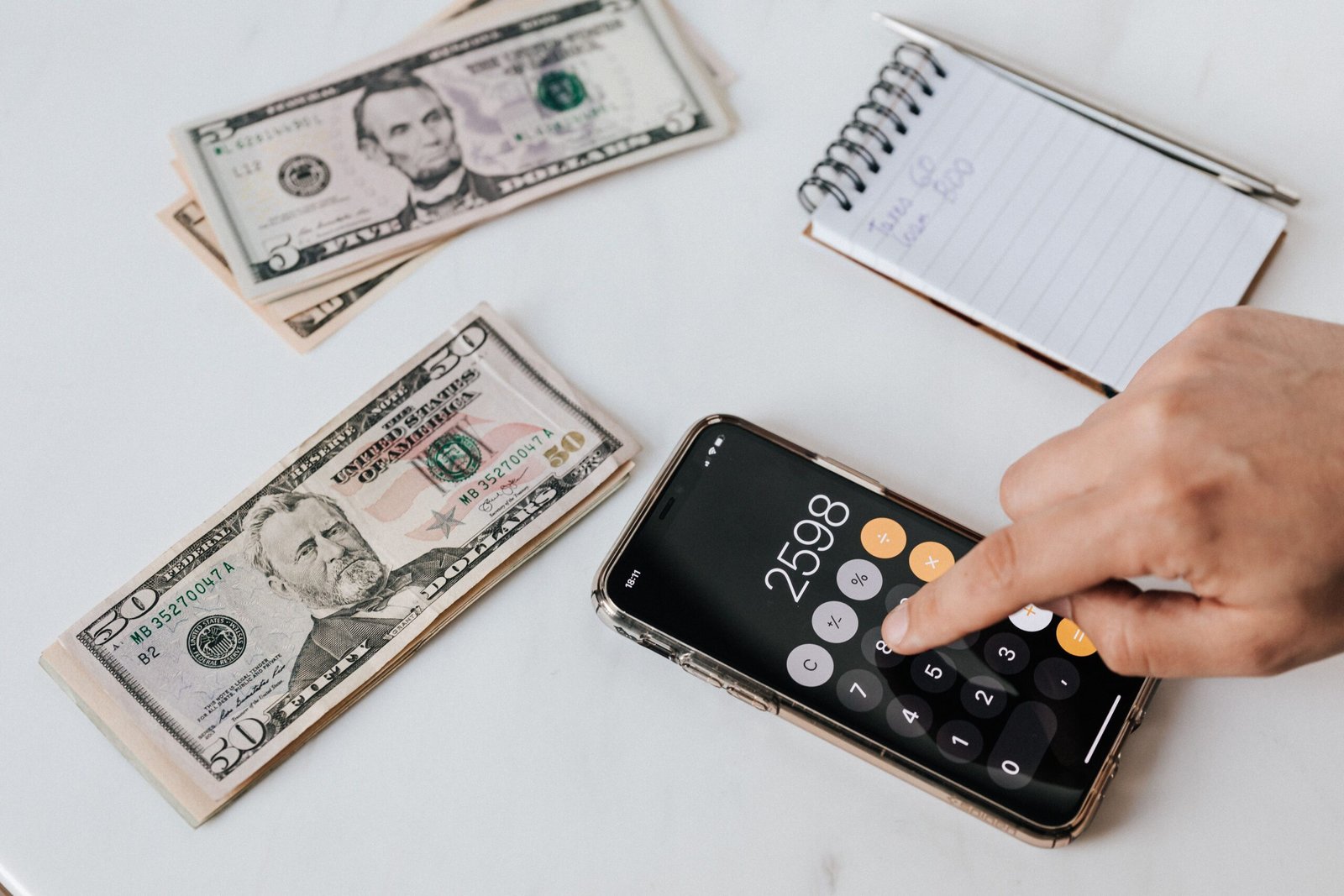 Hand using a calculator with cash and notebook to calculate a freelance day rate