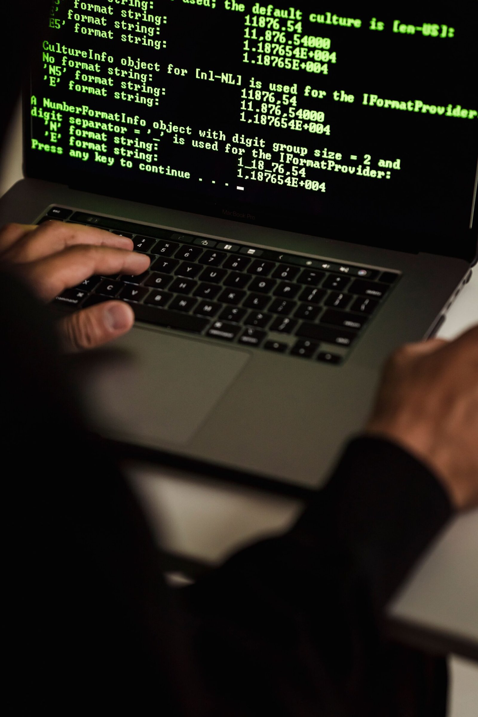 Close-up of hands typing on a laptop with code on screen, representing phishing attack awareness at work