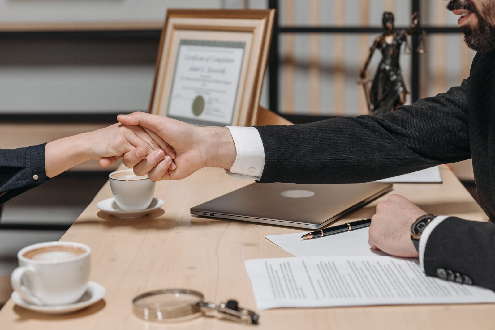 Two business professionals shaking hands with documents on the desk, representing properly terminating a supplier contract